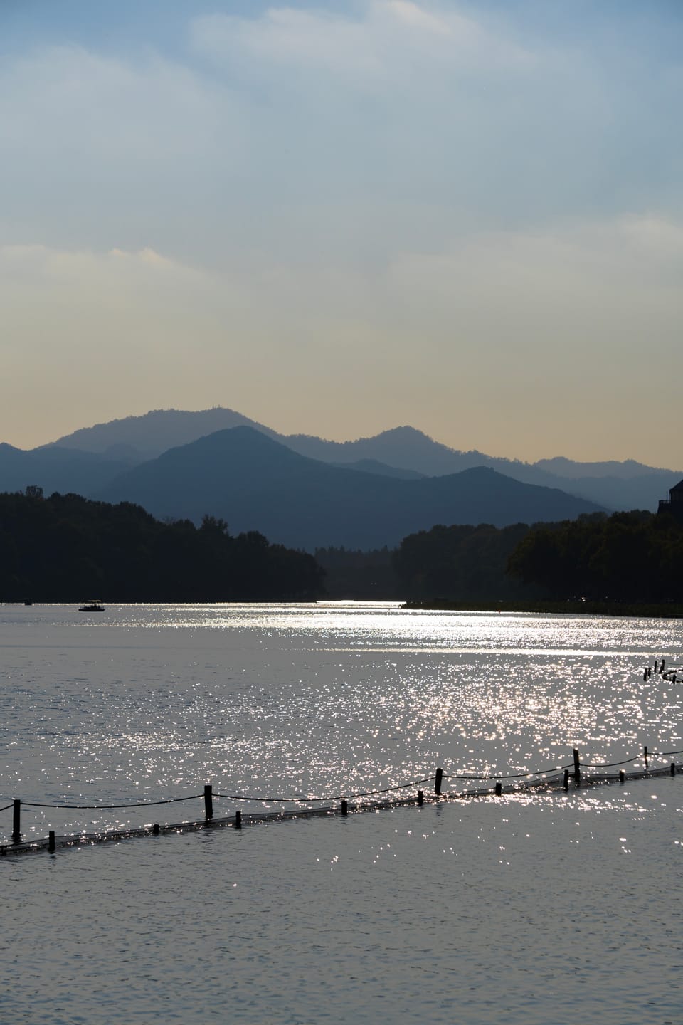 逆光湖面波光粼粼，远处层叠山峦与岸边树林