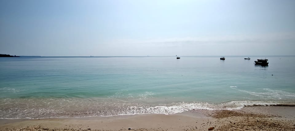 平静海湾的沙滩与远处停泊的渔船